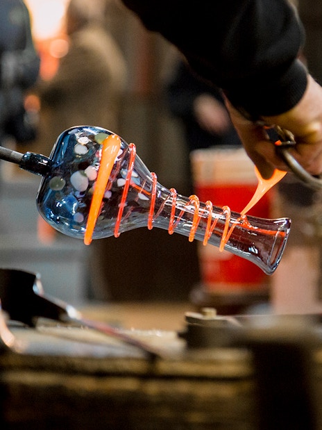 Artisan crafting glass vase in Murano workshop.