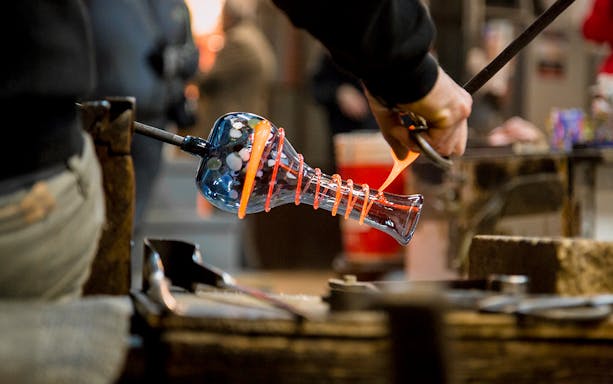 Artisan crafting glass vase in Murano workshop.