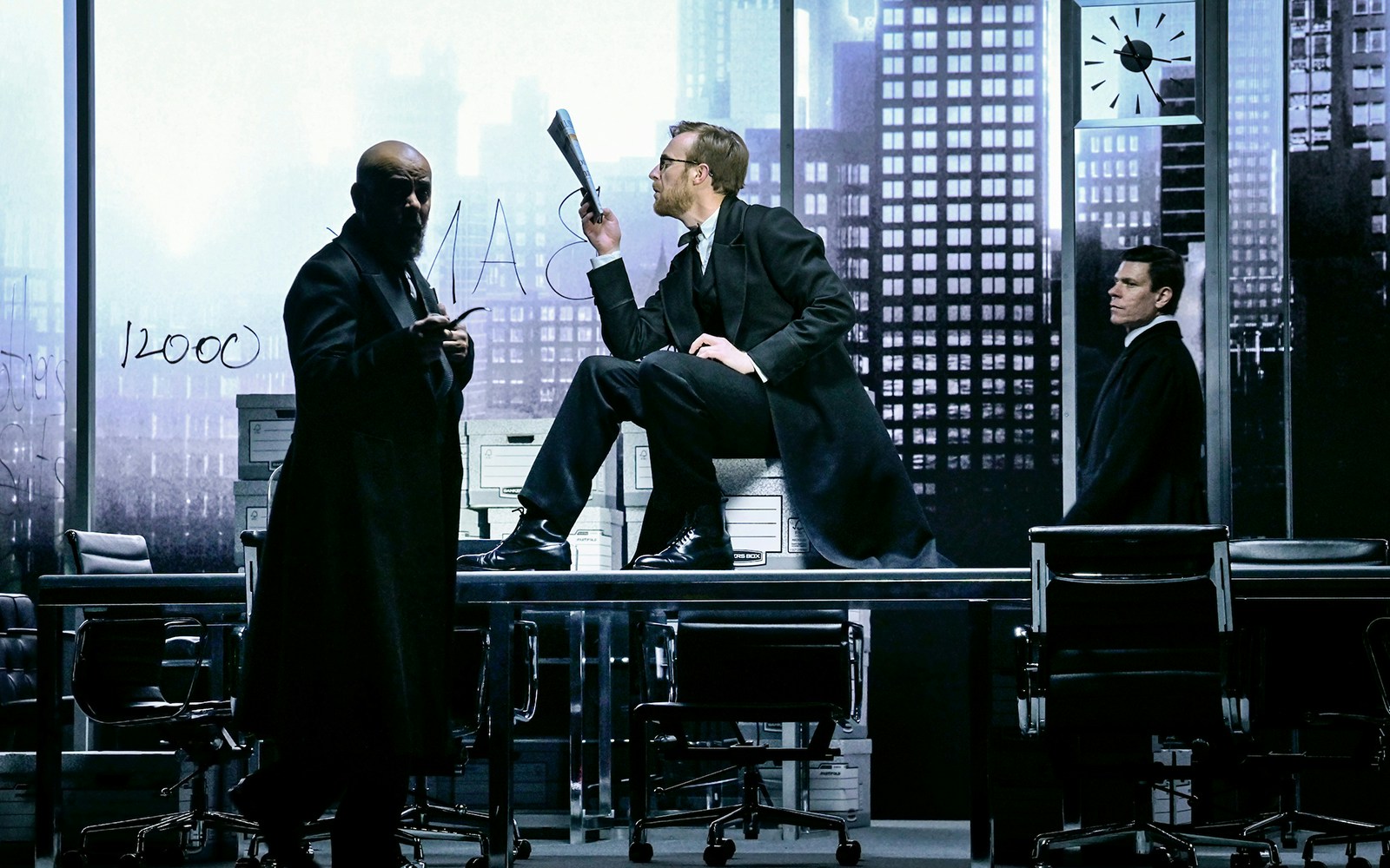 Actors performing "The Lehman Trilogy" on stage with a cityscape backdrop.