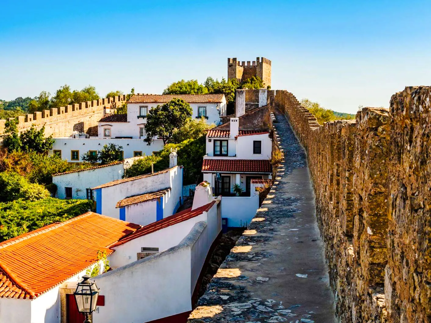 Stone walls and traditional houses in Óbidos, Portugal, with a view of the historic castle.
