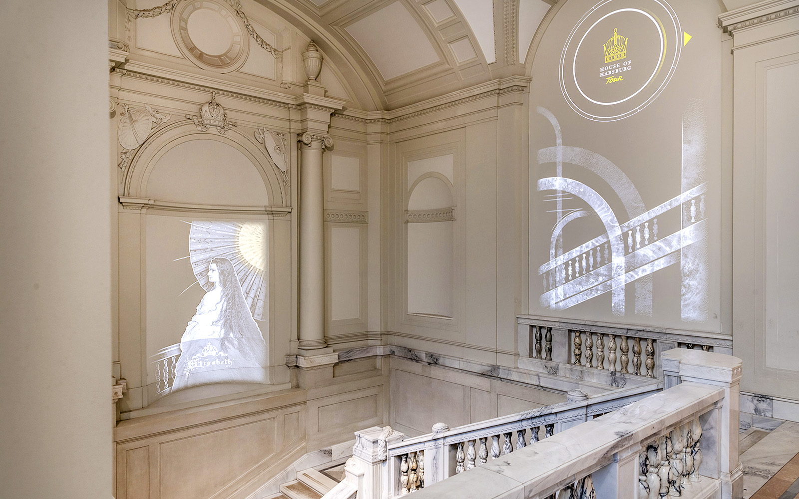 Staircase inside New Hofburg Palace with projected artwork and architectural details.