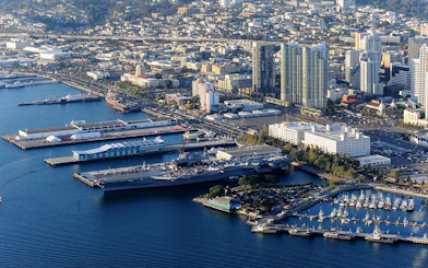 USS Midway Museum aircraft carrier docked in San Diego harbor with city skyline.
