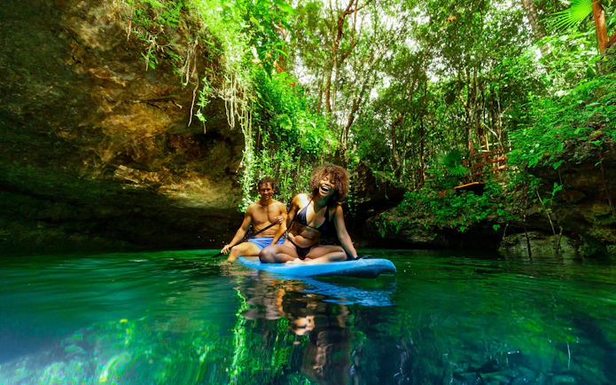 Paddleboarding in a lush cenote during Cancun Extreme Adventure tour.