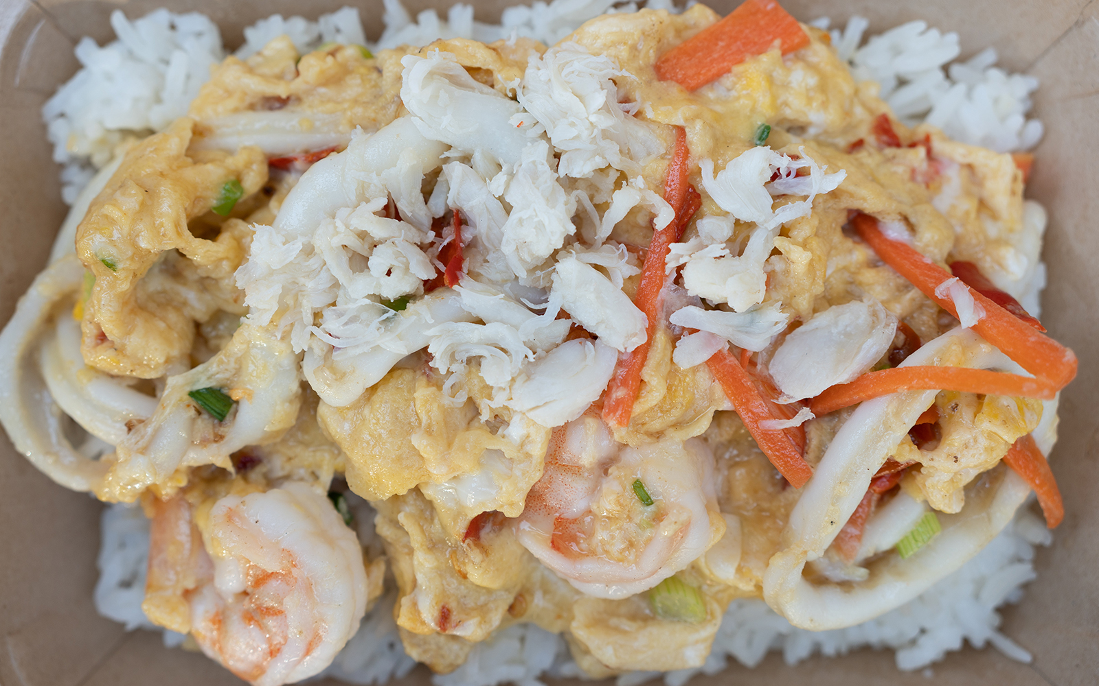 Seafood egg scrambled topped with shrimp, squid and crab meat on rice in brown box