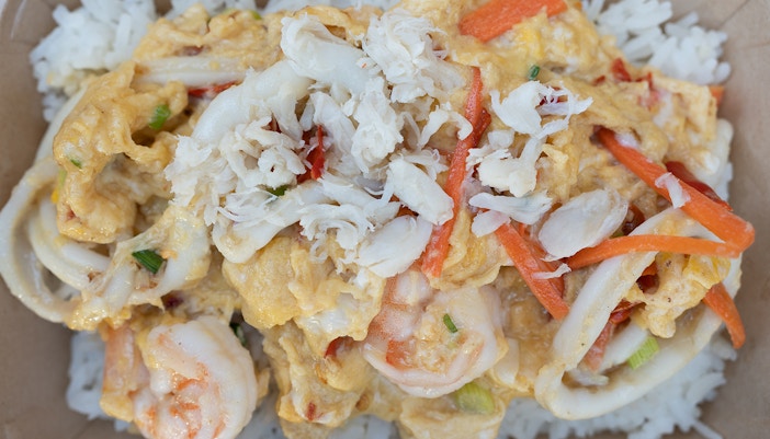 Seafood egg scrambled topped with shrimp, squid and crab meat on rice in brown box