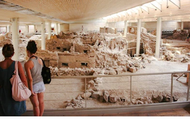 Visitors viewing Akrotiri Bronze Age ruins, Santorini archaeological site.