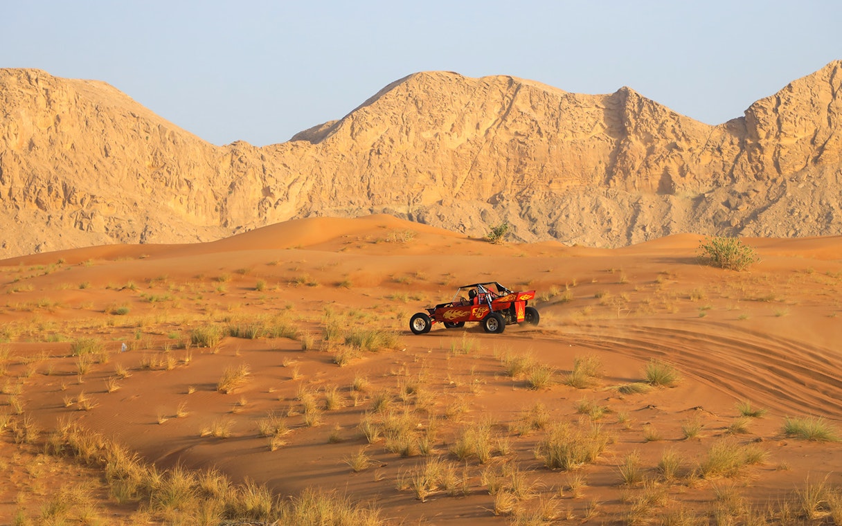 Dune buggy driving through Dubai's Red Dunes desert with rocky mountains in the background.