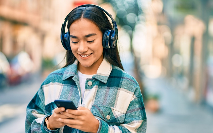I don't know who this is, but here's the alt text:
"Person listening to music on headphones while using a smartphone outdoors.