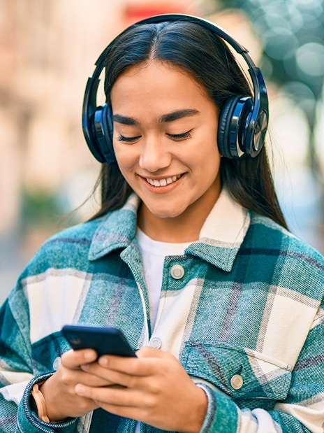 I don't know who this is, but here's the alt text:
"Person listening to music on headphones while using a smartphone outdoors.