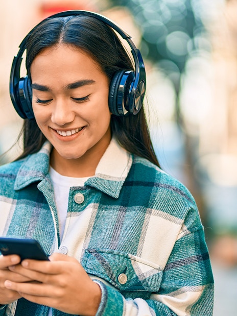 I don't know who this is, but here's the alt text:
"Person listening to music on headphones while using a smartphone outdoors.