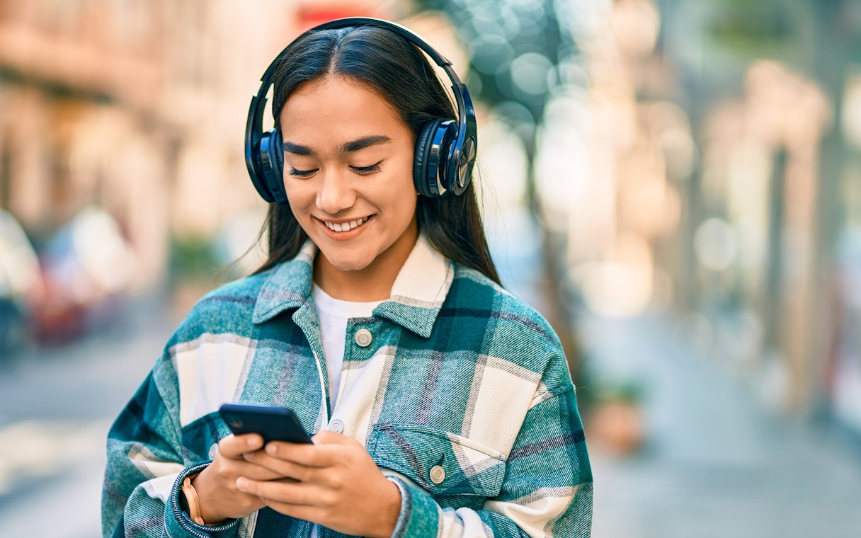I don't know who this is, but here's the alt text:
"Person listening to music on headphones while using a smartphone outdoors.