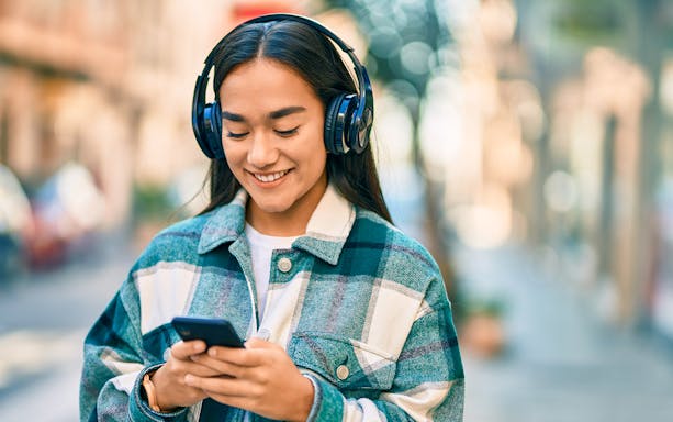 I don't know who this is, but here's the alt text:
"Person listening to music on headphones while using a smartphone outdoors.