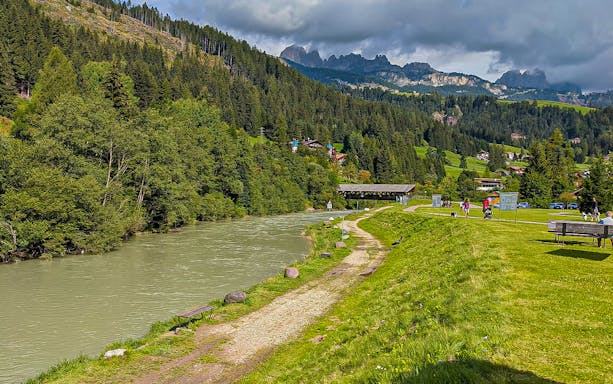 Pathway along a river with Dolomites in the background, part of a guided tour from Lake Garda.