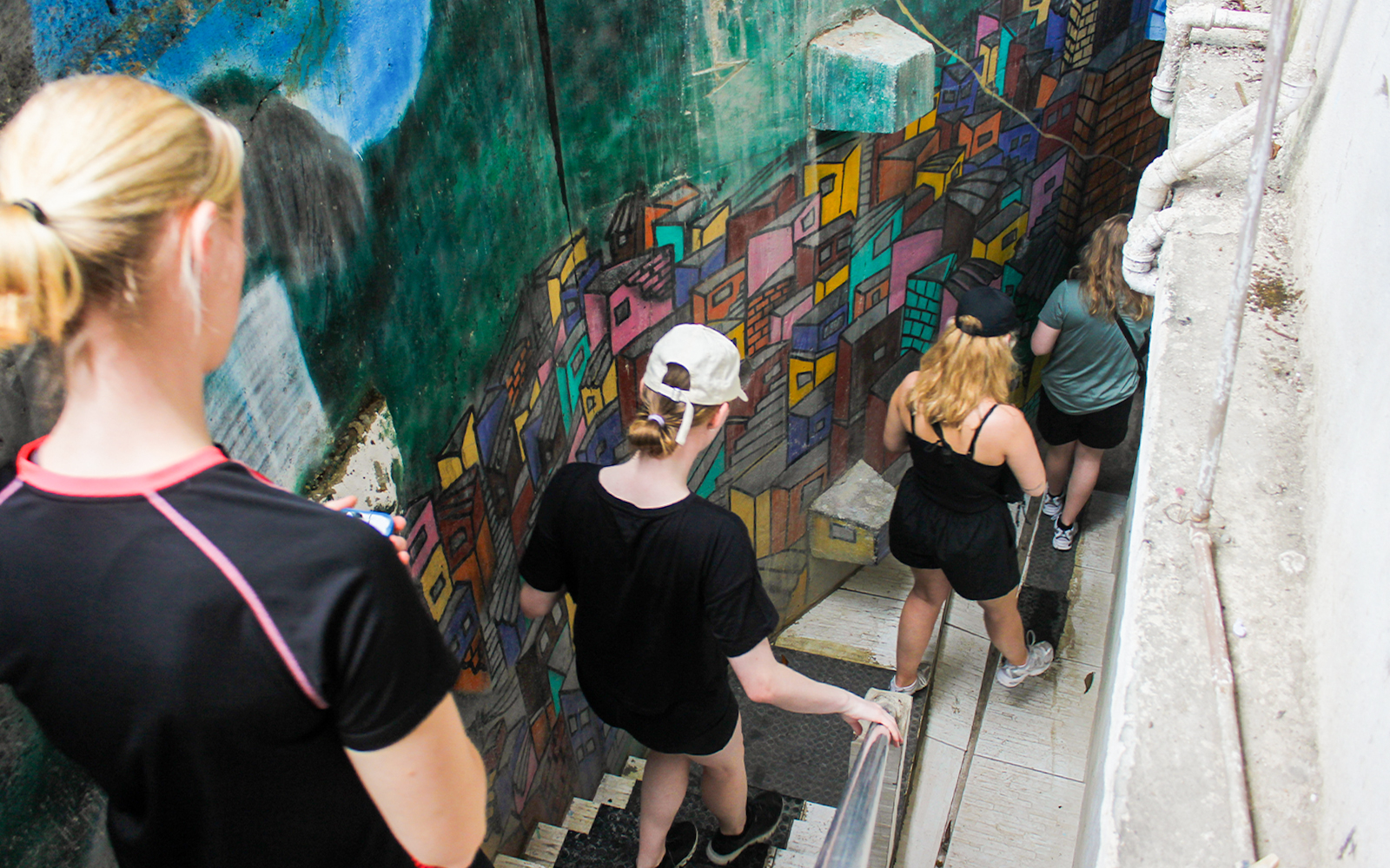 Tourists walking down colorful mural-lined stairs in a Rio favela.