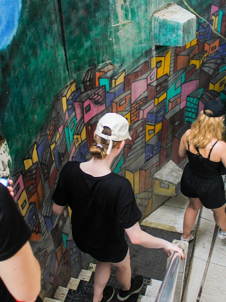 Tourists walking down colorful mural-lined stairs in a Rio favela.
