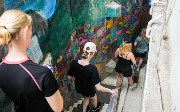 Tourists walking down colorful mural-lined stairs in a Rio favela.