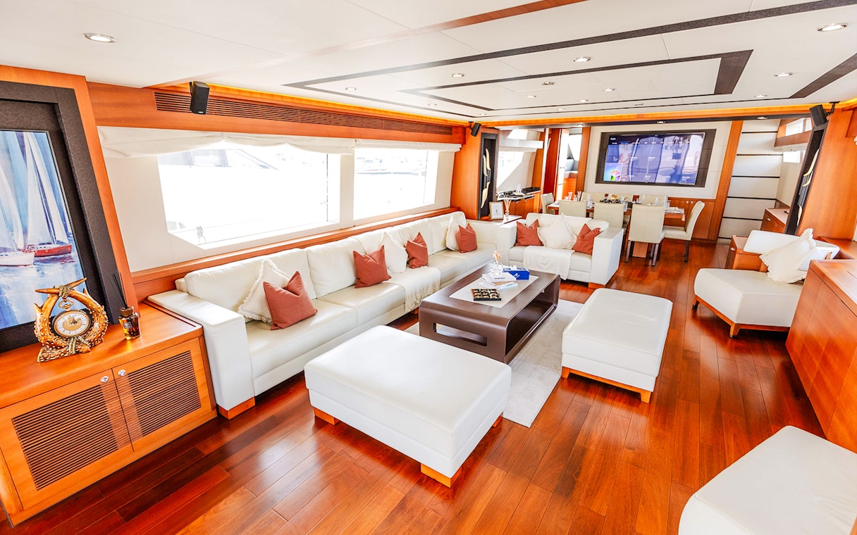 Luxurious yacht interior with white leather seating, wooden flooring, and a dining area.