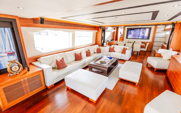 Luxurious yacht interior with white leather seating, wooden flooring, and a dining area.