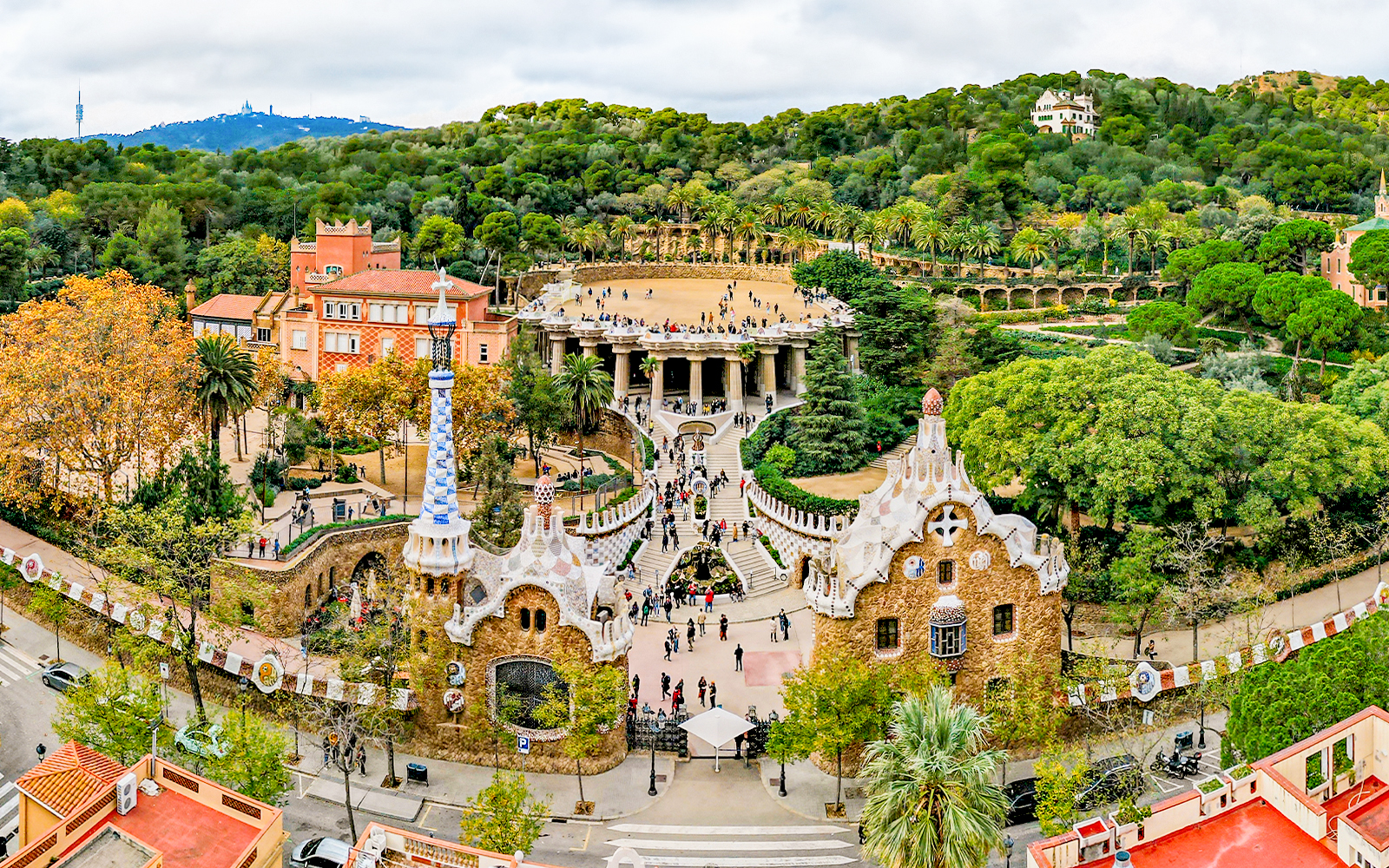 Aerial view of Park Güell in Barcelona, showcasing colorful mosaic structures and lush gardens.