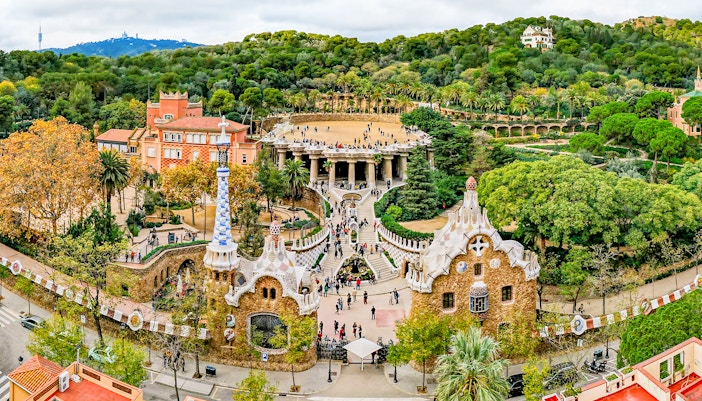 Aerial view of Park Güell in Barcelona, showcasing colorful mosaic structures and lush gardens.