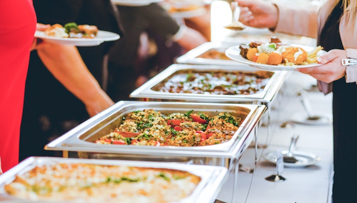 Buffet with various dishes and people serving themselves.