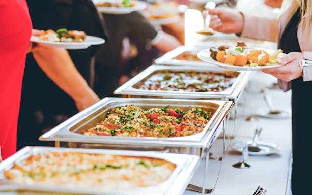 Buffet with various dishes and people serving themselves.