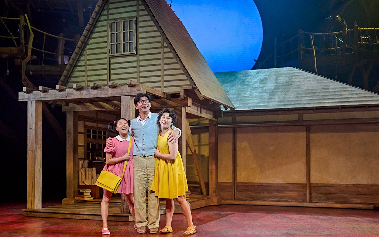 Stage scene from My Neighbour Totoro show in West End with three actors in front of a house set.