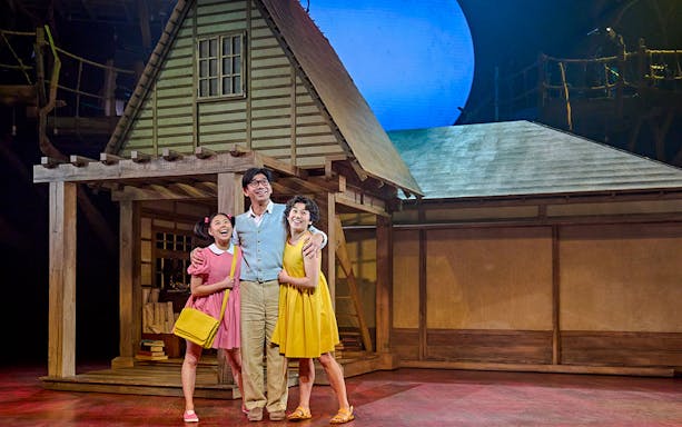 Stage scene from My Neighbour Totoro show in West End with three actors in front of a house set.