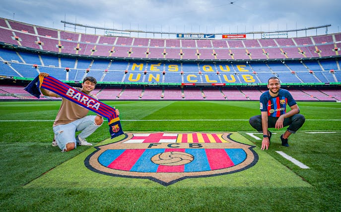 Fans at FC Barcelona's Camp Nou stadium with team scarf and emblem.