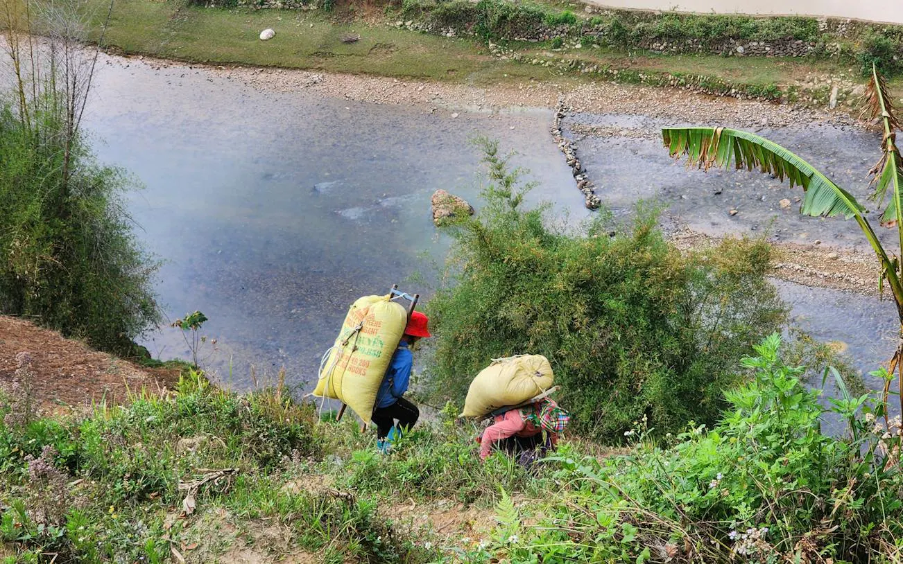People carrying sacks along a riverbank in Mu Cang Chai, Vietnam.