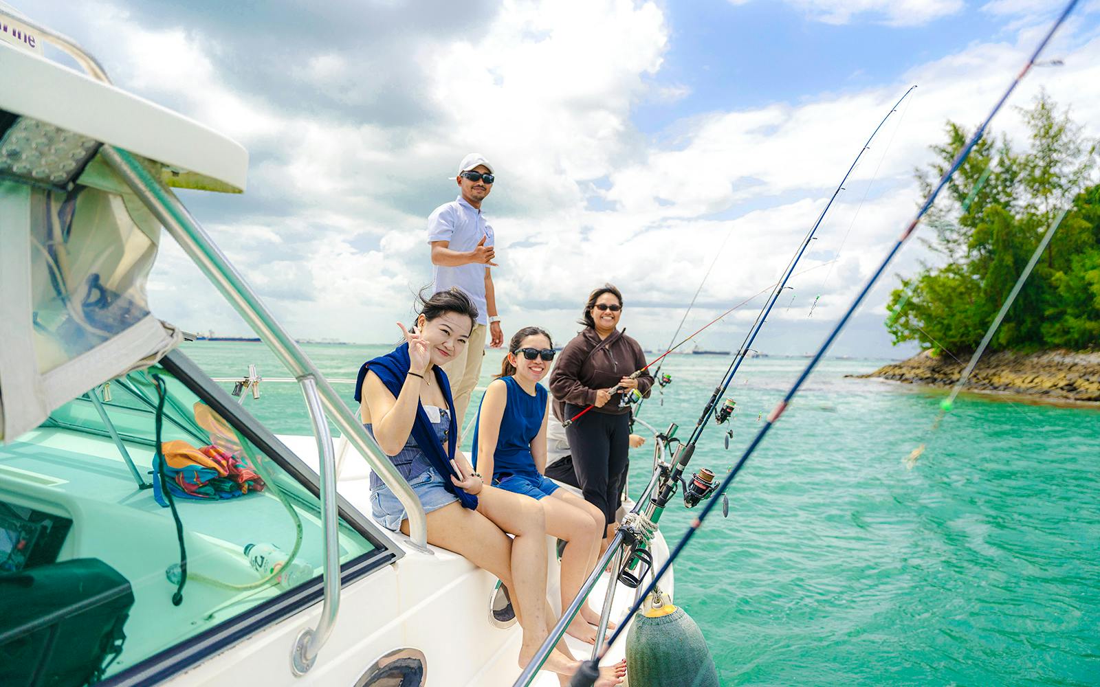 Group fishing on a yacht in turquoise waters near a lush shoreline.