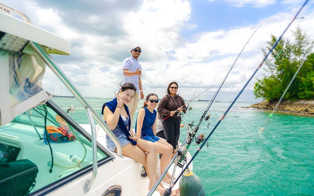 Group fishing on a yacht in turquoise waters near a lush shoreline.