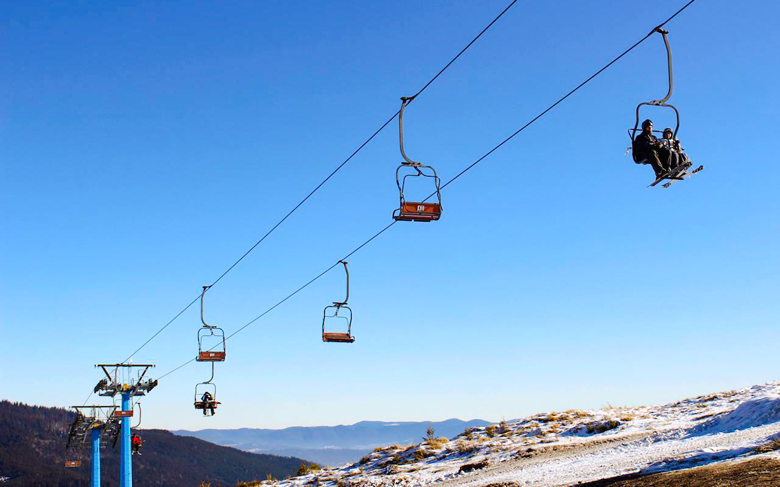Ski lift ascending Mt Buller, Australia with skiers seated against a clear blue sky.