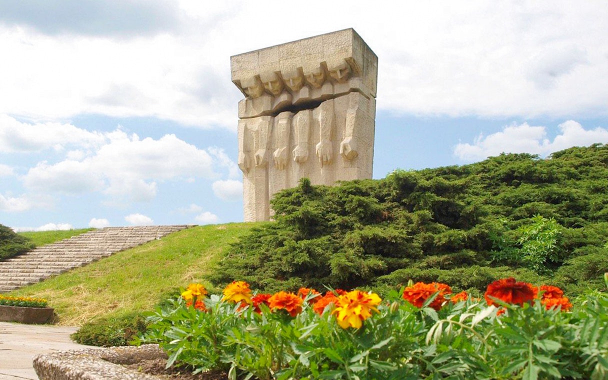 Monument to the Victims of Fascism Plaszow in Krakow with surrounding greenery and flowers.