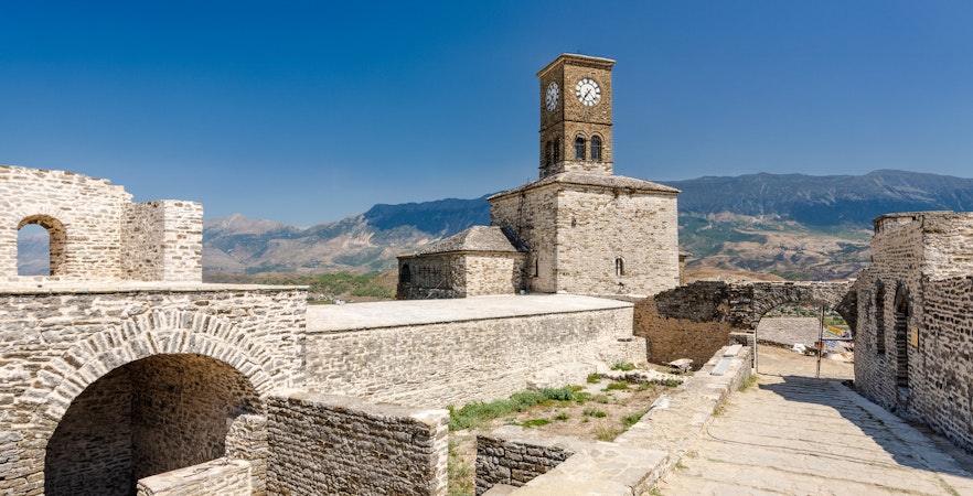 Clock tower at Gjirokaster castle with mountain backdrop.
