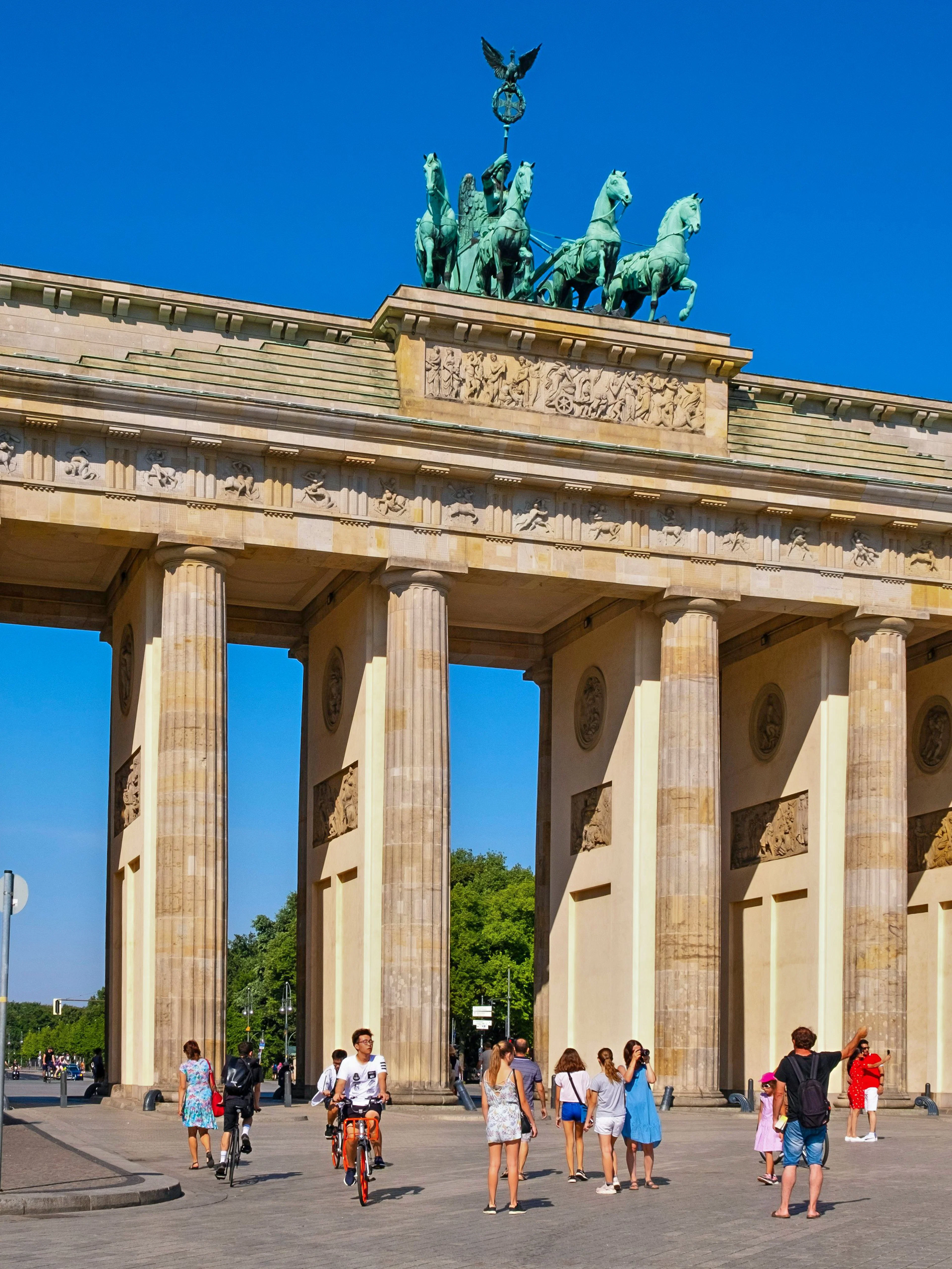 Brandenburg Gate at Pariser Platz, Berlin, with tourists walking and cycling nearby.