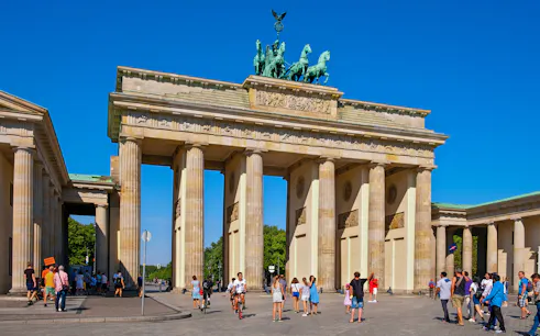 Brandenburg Gate at Pariser Platz, Berlin, with tourists walking and cycling nearby.