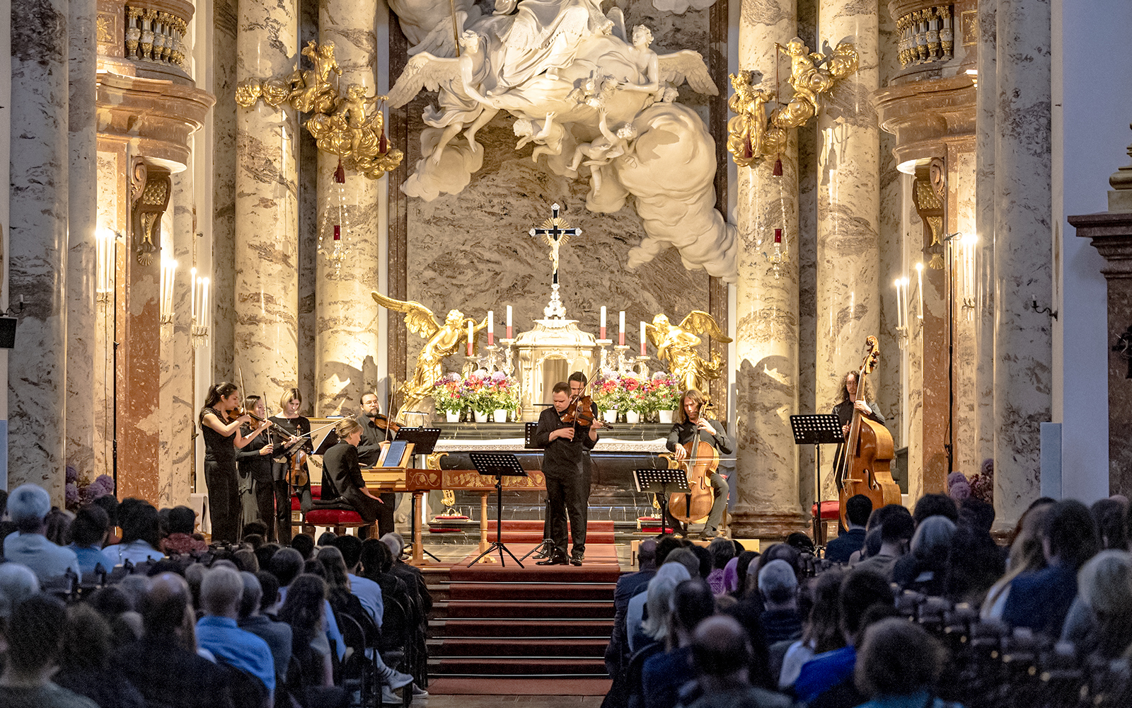 Musicians performing Vivaldi's Four Seasons in an ornate concert hall.