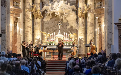 Musicians performing Vivaldi's Four Seasons in an ornate concert hall.