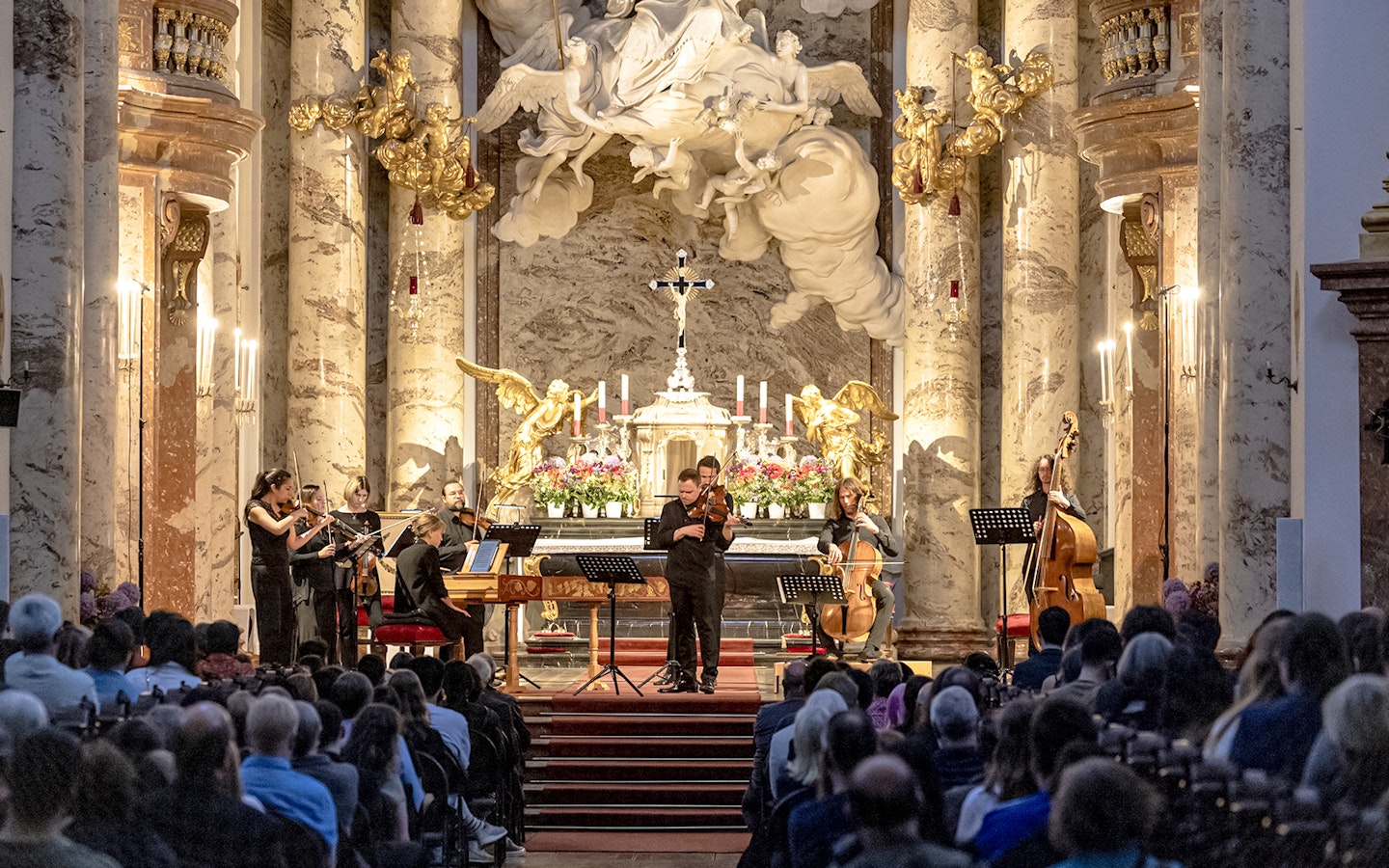 Musicians performing Vivaldi's Four Seasons in an ornate concert hall.