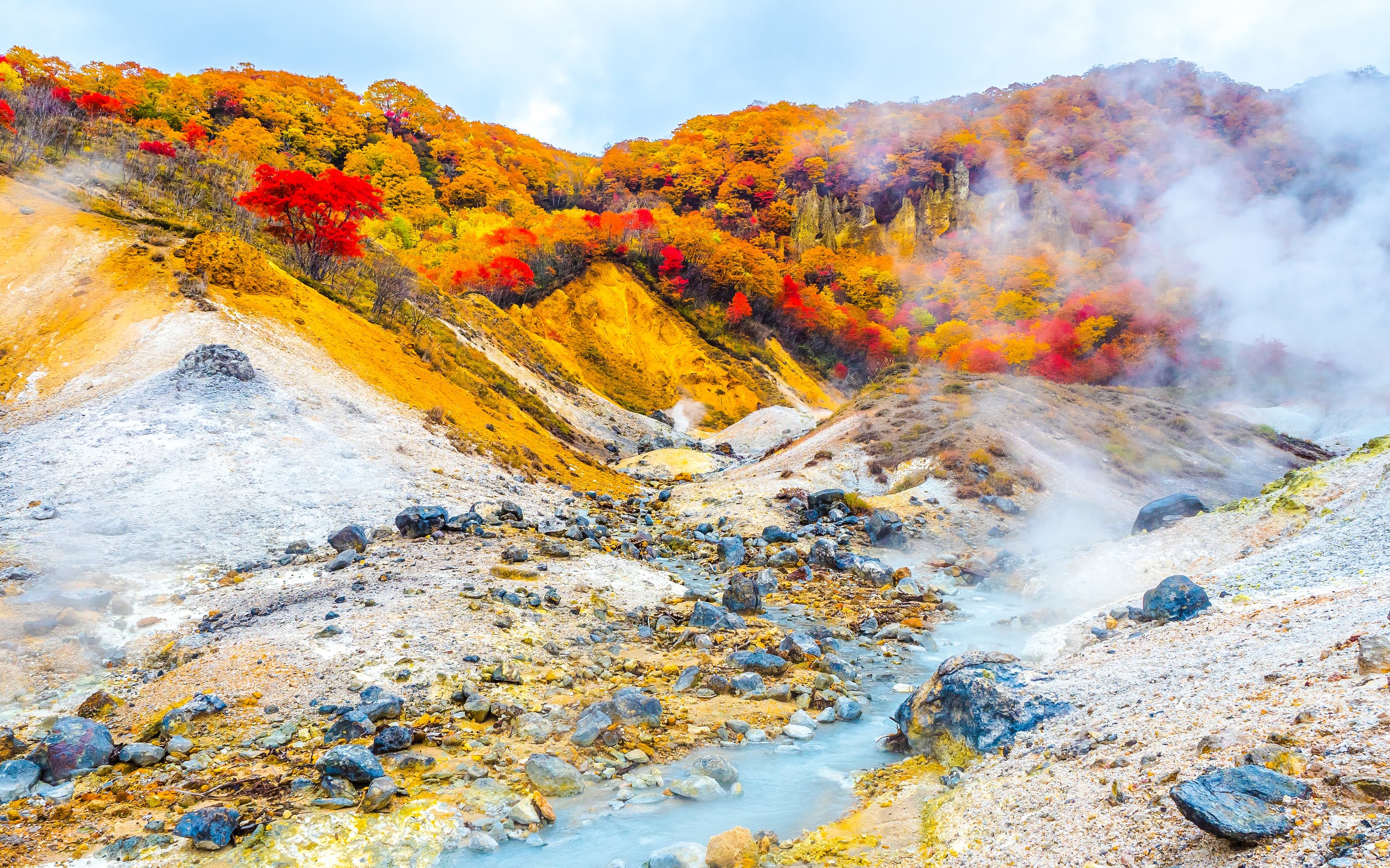 Steaming hot springs with colorful autumn foliage in Noboribetsu Onsen, Japan.