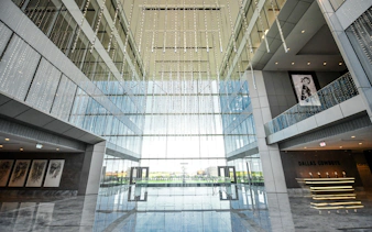 Multi-level corporate atrium with glass walls and hanging lights, Dallas Cowboys signage visible.