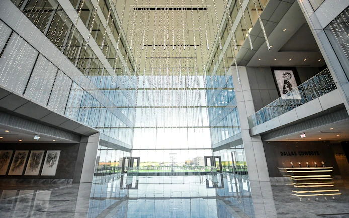 Multi-level corporate atrium with glass walls and hanging lights, Dallas Cowboys signage visible.