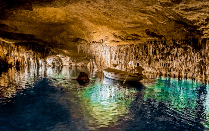 Boat tour inside Drach Caves with stalactites and illuminated water reflections.