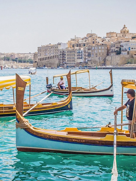 Traditional boats on the water with a view of the Three Fortified Cities in Malta.