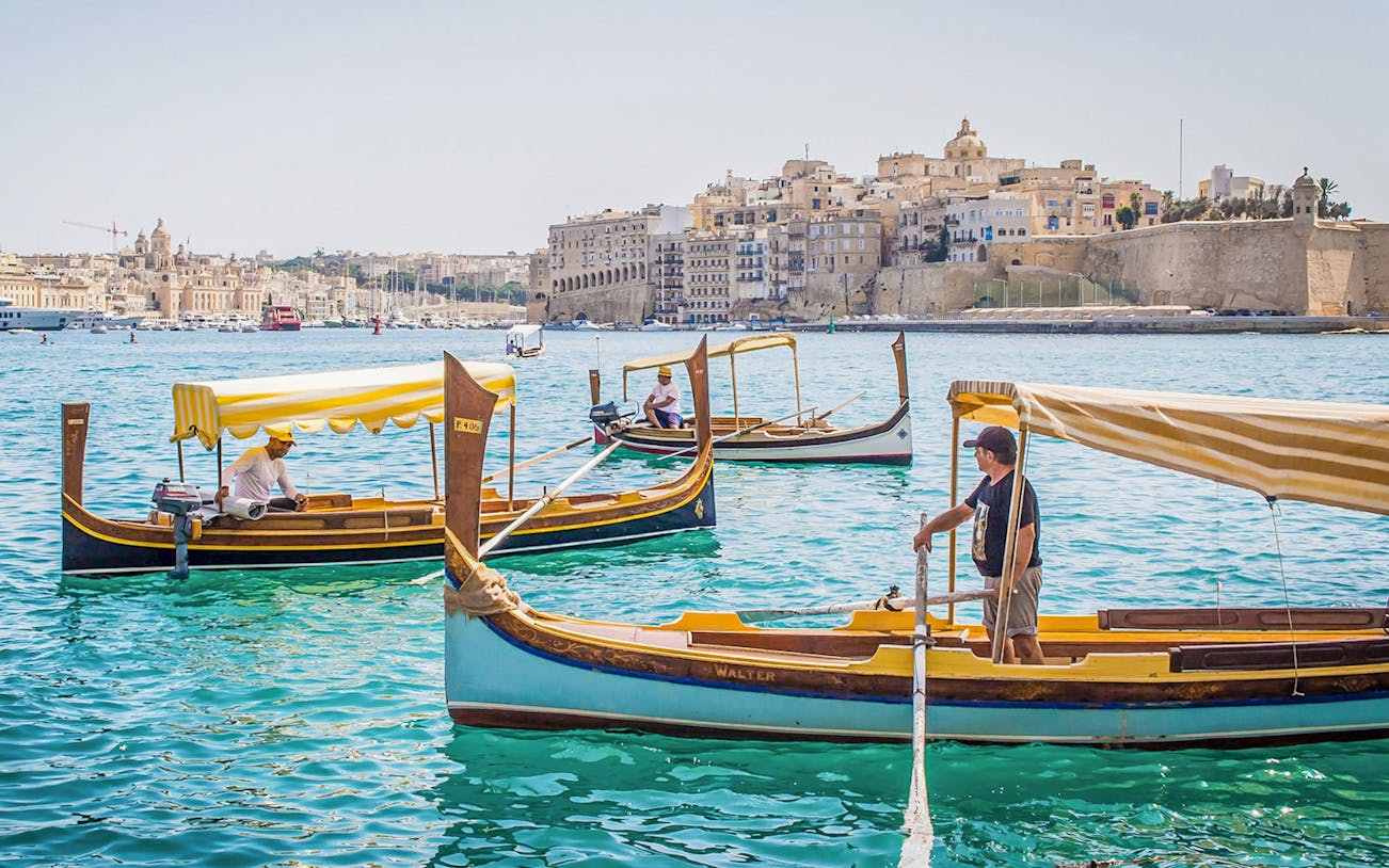Traditional boats on the water with a view of the Three Fortified Cities in Malta.