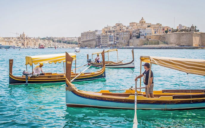 Traditional boats on the water with a view of the Three Fortified Cities in Malta.