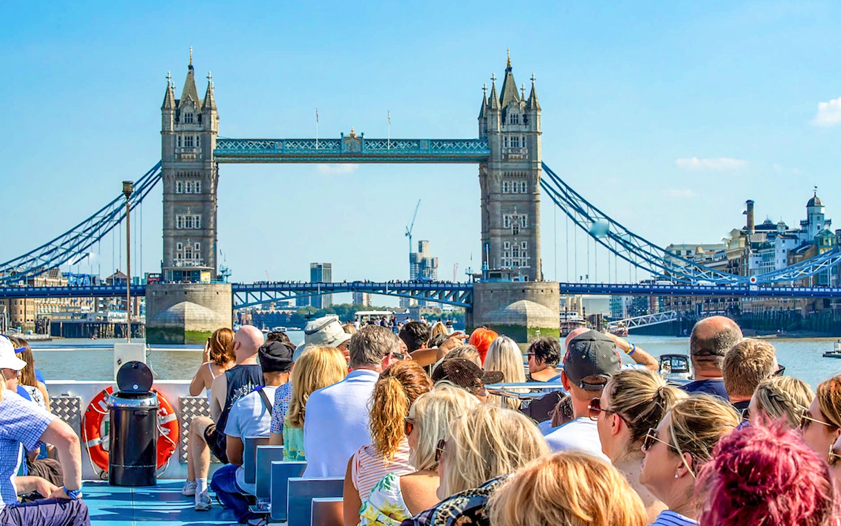 Sightseeing cruise passengers view Tower Bridge on the Thames in London.