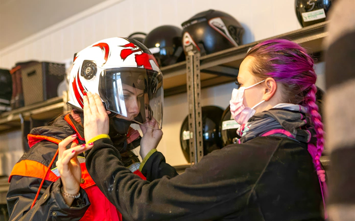 Guest preparing for a snowmobile ride in Tromsø with helmet fitting assistance.
