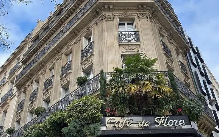 Café de Flore facade in Saint-Germain-des-Prés, Paris, with ornate balconies and greenery.